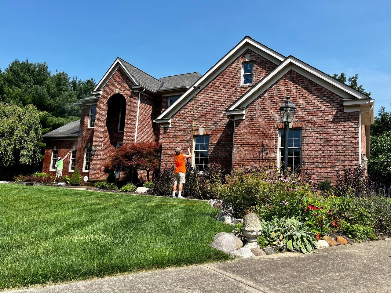 Two Central Window Cleaning technicians washing windows on a brick residential home, Akron OH area