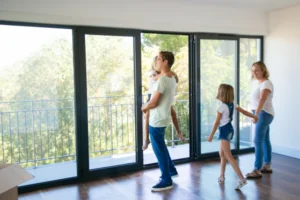 Family looking at house with large glass doors in empty living room.