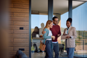 Couple speaking to woman outside of house with large windows.